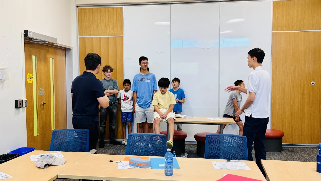 Students standing at a whiteboard during a Young Economists session while one of the mentors talks them through it.